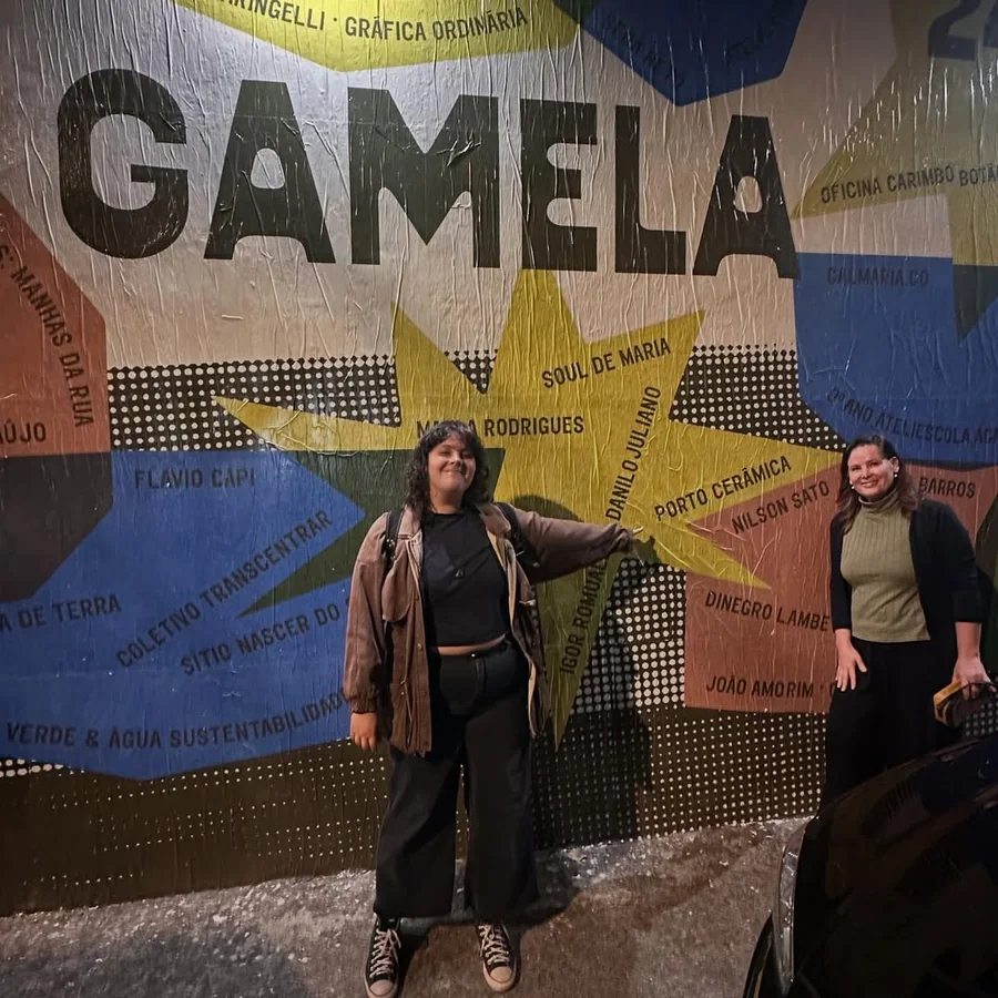 Duas pessoas em frente a um mural pintado com a palavra Gamela, à noite