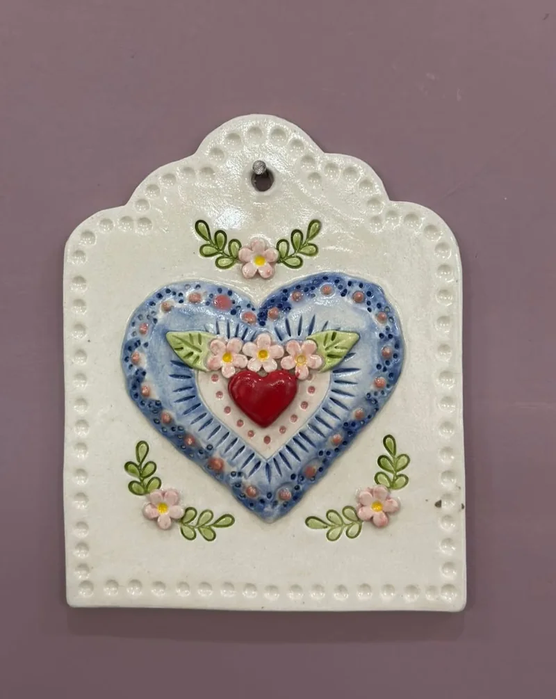 Plaquinha de cerâmica em forma de etiqueta, com um coração azul e flores em relevo