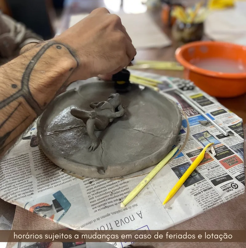 Mãos abrindo a argila no torno, sobre jornal
